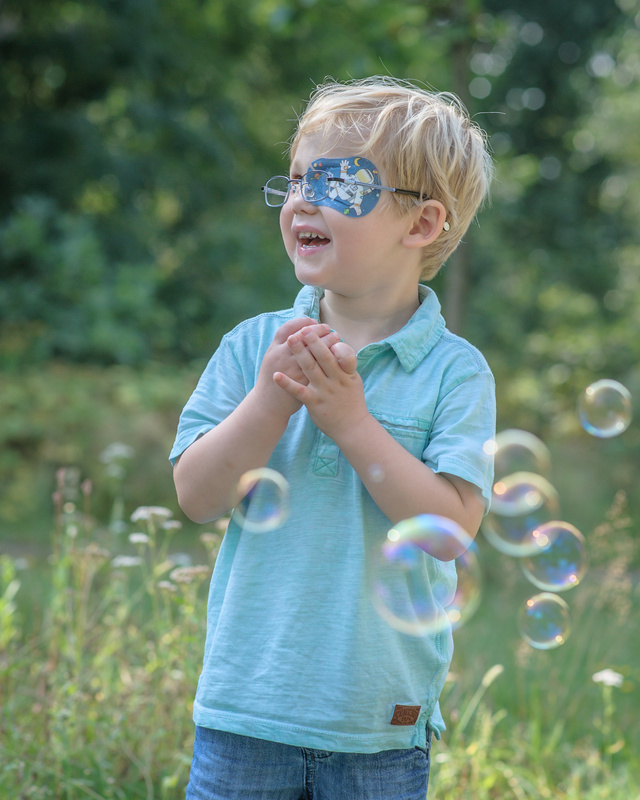 Kleiner Junge auf Wiese macht Seifenblasen und trägt das ORTOPAD® Augenpflaster "Astronaut"