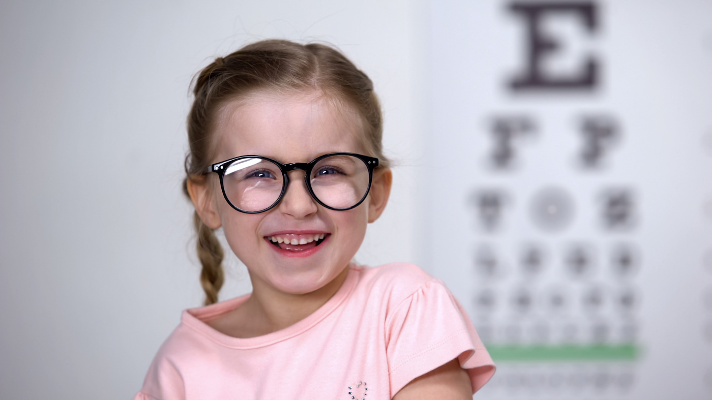 Lachendes Mädchen mit Brille vor Sehtafel